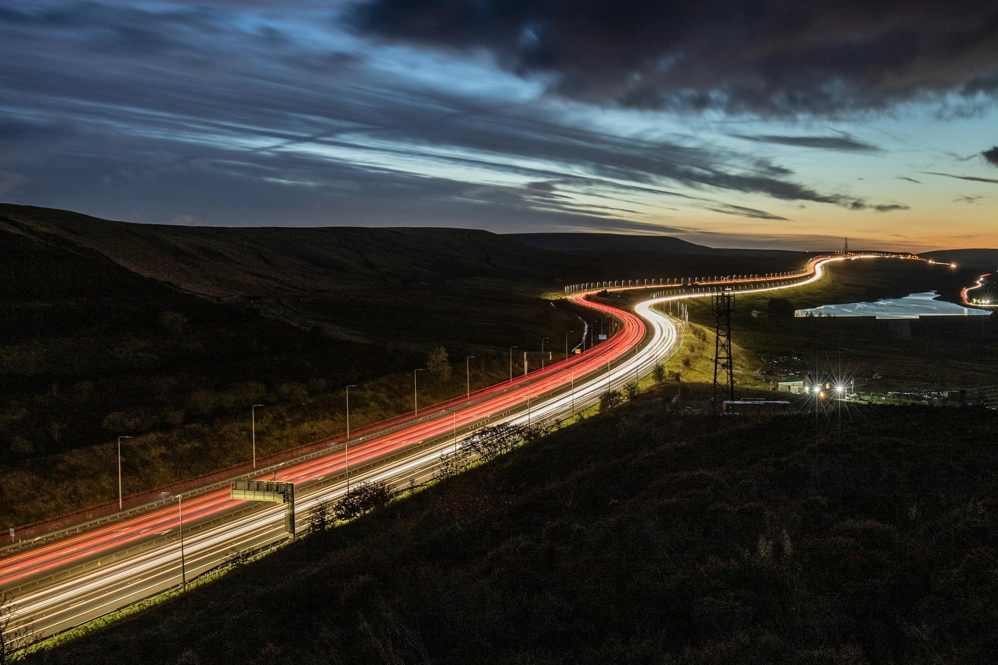 A motorway winding through dark moorland at dusk, lit by headlights