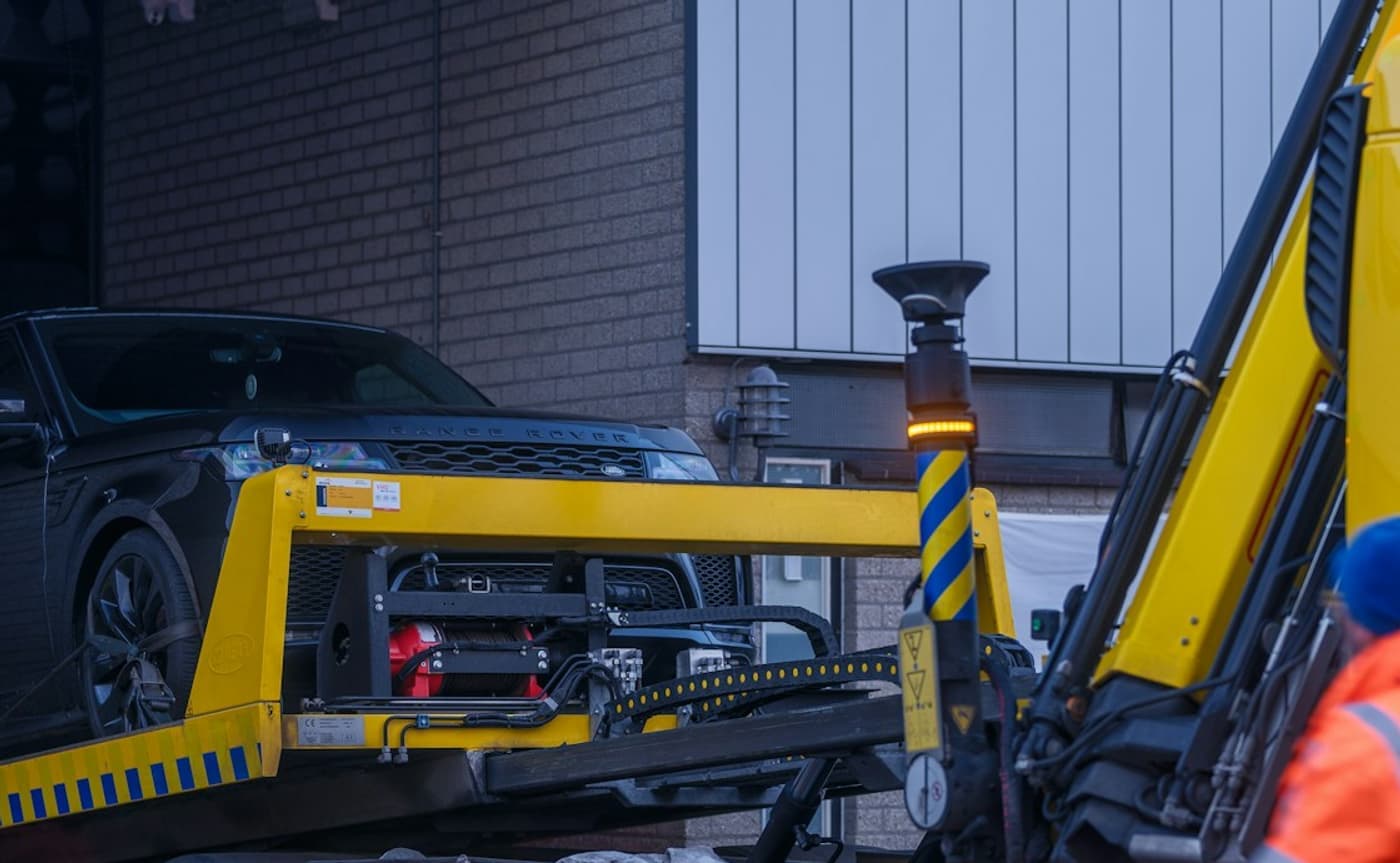 A recovery truck bed tilted while a black Range Rover is winched aboard